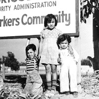 Farm worker children in front of a sign for a government migrant worker community