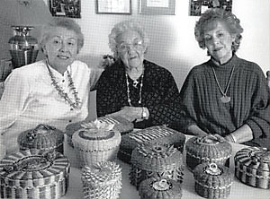 Photo of three women sitting behind a table covered with baskets