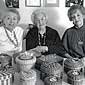 Photo of three women sitting behind a table covered with baskets