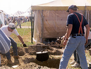 Photo of two men holding a pole with pot over a hole in the ground