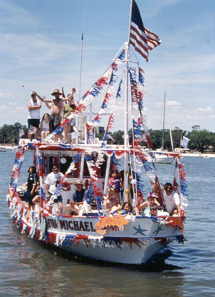 Photo of shrimp boat with people, a flag, and red, white, and blue streamers