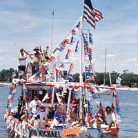 Photo of shrimp boat with people, a flag, and red, white, and blue streamers