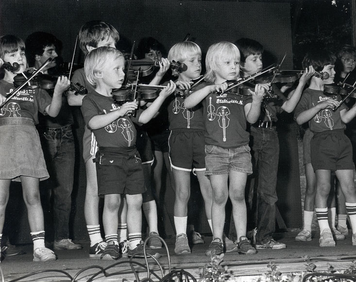 Photo of young children playing fiddles on stage