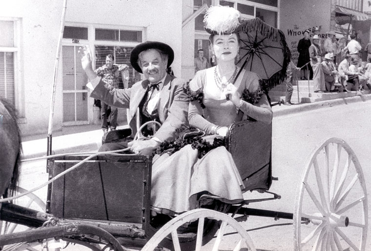 Photo of man and woman in period dress in a horse drawn carriage in a parade