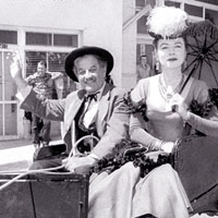 Photo of man and woman in period dress in a horse drawn carriage in a parade