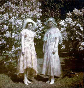 Photo of two women wearing dresses in front of lilacs
