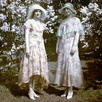 Photo of two women wearing dresses in front of lilacs