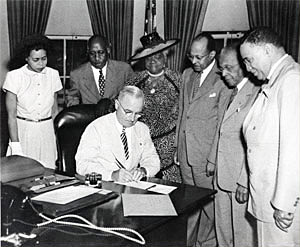 Photo of President Harry Truman signing with six people watching