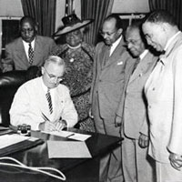 Photo of President Harry Truman signing with six people watching