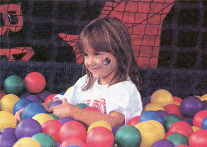 Photo of a young girl surrounded by brightly colored plastic balls