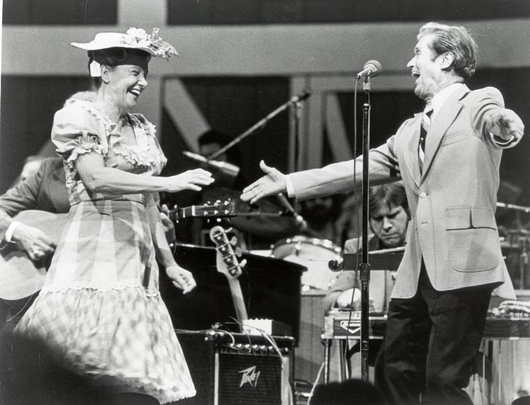 Photo of Minnie Pearl and Roy Acuff dancing and singing in front of a band