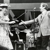 Photo of Minnie Pearl and Roy Acuff dancing and singing in front of a band