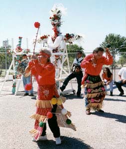 Photo of Los Matachines dancing in front of a cross