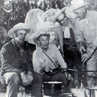 Photo of four men in cowboy hats cooking outside