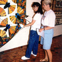 Photo of two women looking at labels on displayed quilts