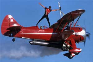 Photo of man standing on the top of a red biplane while pilot flies