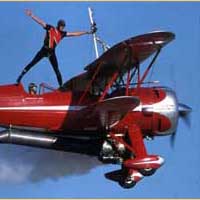 Photo of man standing on the top of a red biplane while pilot flies