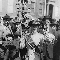 Suffragist, 'Mrs. Suffern,' holding sign; crowd of boys and men behind.