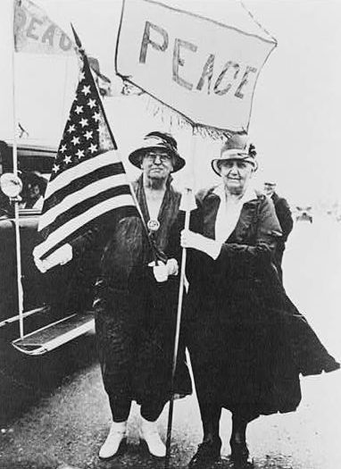 Jane Addams and Mary McDowell(?), full-length portrait, standing, holding U.S. flag and peace banner