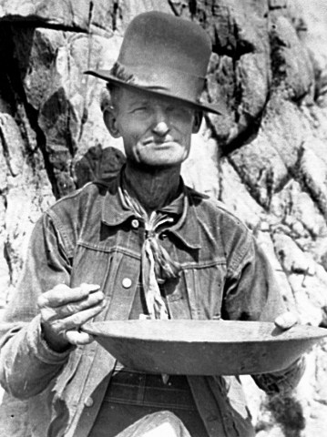 Photo of a miner holding a pan and a piece of gold.