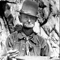 Photo of a miner holding a pan and a piece of gold.