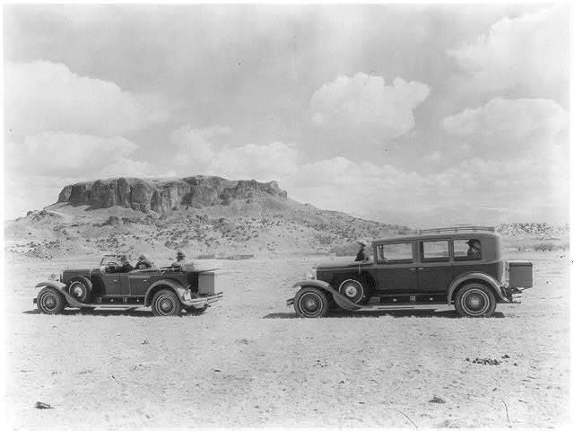 Side view of two automobiles, one a convertible, with Black Mesa, Arizona in the background, ca. 1924.