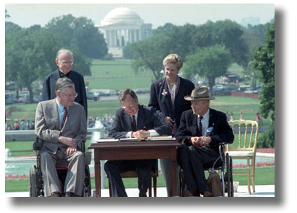 1990年《美國殘疾人法》簽署儀式。坐在第一任布希總統(中)兩側的分別是平等就業機會委員會主席肯普(左)和總統殘疾人就業委員會主席達特。站立者為威爾克牧師(左)和全國殘疾人事務委員會會長斯威夫特(右)。