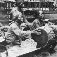 Black and white photo of people sitting on ground behind a stage