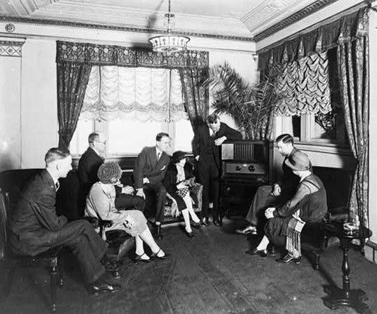 Atwater Kent, standing by radio, and seven other people listening to the radio