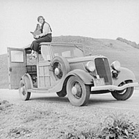 Photographer Dorothea Lange sitting on top of car with her camera in California