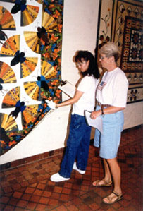 Photo of two women looking at labels on displayed quilts